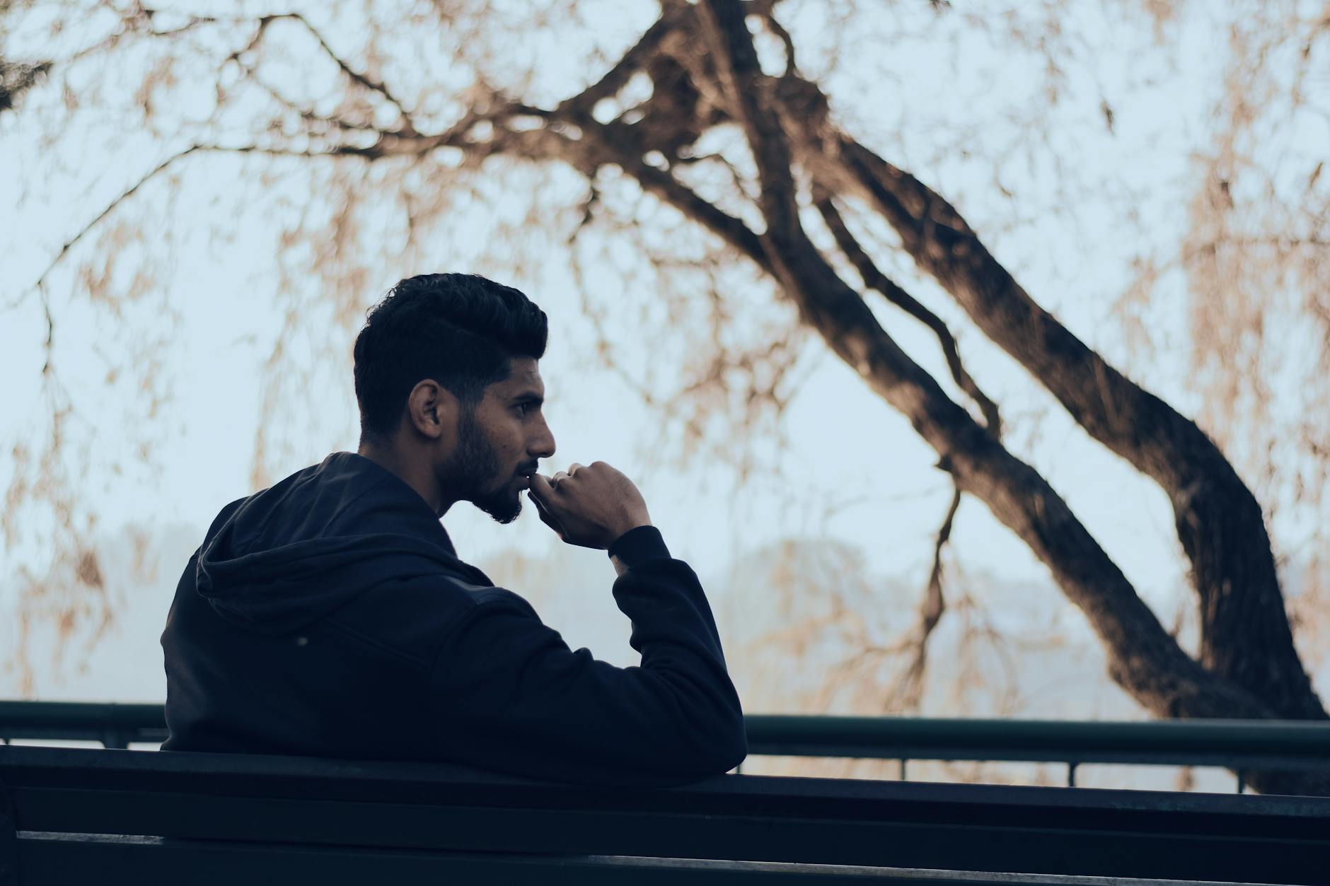 man in black hoodie sitting on bench near green trees