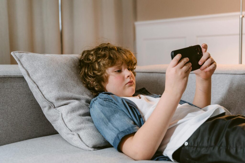 a boy using a smartphone while lying on a sofa